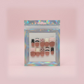 A packaged set of nail art designs on a wooden surface with a cup and other items in the background.